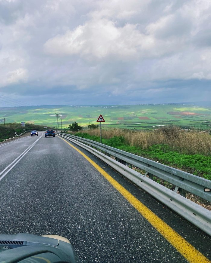A road winding down into a green valley on a cloudy winter day